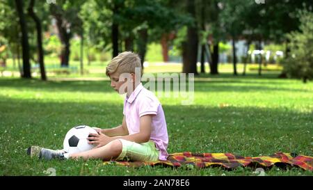 Triste ragazzo seduto in posizione di parcheggio con il calcio, mancanza di amici, vittima di bullismo Foto Stock