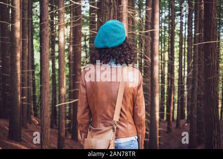 Donna che indossa una giacca di pelle marrone e verde piana-round hat guardando la foresta di alberi Foto Stock