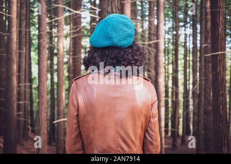 Donna che indossa una giacca di pelle marrone e verde piana-round hat guardando la foresta di alberi Foto Stock