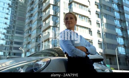 Fiducioso lady in business suit in piedi poggiando sulla nuova vettura, il successo e il benessere Foto Stock