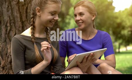 Felice la figlia e la madre lo shopping online nel parco, utilizzando tablet, le vendite nei negozi Foto Stock