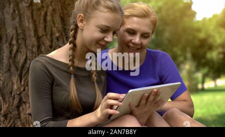 Figlia di madre mostra le foto del suo ragazzo utilizzando tablet, social networking Foto Stock