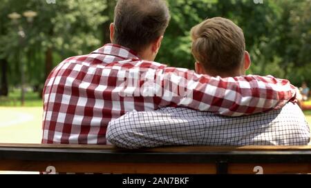 Papà e figlio che abbraccia, seduti su una panchina nel parco, relazioni di sostegno e fiducia Foto Stock