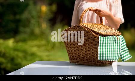 Signora mettendo un cestino picnic su tavola, preparazione per la cena in famiglia all'aperto Foto Stock