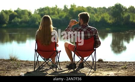 Giovane seduto e godendo splendido fiume scape, uomo di bere birra, tossicodipendenza Foto Stock