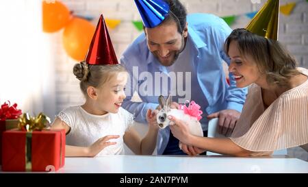 La cura dei genitori rendendo la sorpresa di piccola figlia presentando piccolo simpatico coniglietto Foto Stock