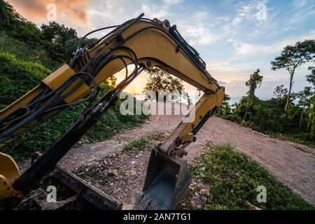 Dettagli di escavatore moderna sul sito della costruzione con il cielo al tramonto. Grande escavatore cingolato in piedi su una collina con un prato verde. Macchinari per un Foto Stock
