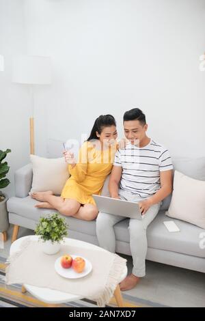Bella donna asiatica e uomo bello rilassarsi sul lettino con il computer portatile e navigare in Internet mentre fare acquisti online Foto Stock