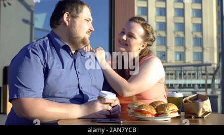 Donna grassa guarda con amore al ragazzo obesi, veri sentimenti, fast food concept Foto Stock