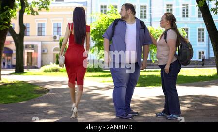 Fat Man guardando bella signora in rosso passando da, obesi fidanzata gelosa Foto Stock