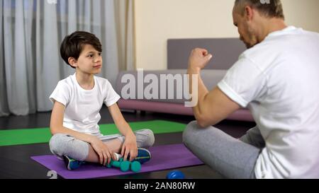 Padre lodando figlio durante home allenamento, insegnamento lui facendo fitness, sport Foto Stock