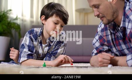 Carefree padre e figlio giocare gioco di bordo, giacente sul piano, happy family concept Foto Stock