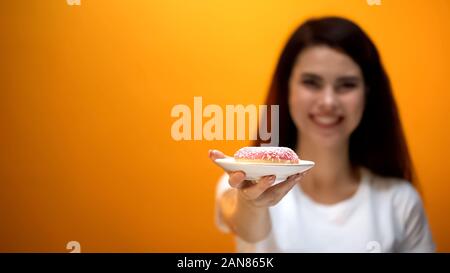Felice ragazza che mostra una deliziosa ciambella alla telecamera, addolciti snack, rischio di obesità Foto Stock