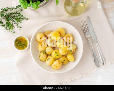 Cotto al forno con spezie tutto tondo i tuberi di patata in piastra bianca su sfondo tessili, golden con crosta, vista dall'alto Foto Stock