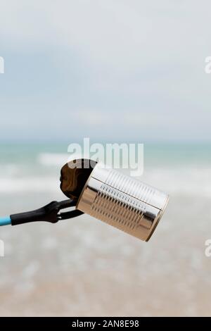 Primo piano della qualcuno raccogliere rifiuti con un estensore di raggiungere, in una spiaggia solitaria, come azione di ripulire l'ambiente naturale Foto Stock