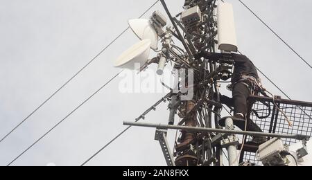 Elettricista uomo o alpinista arrampicata su palo antenna per ispezione Foto Stock