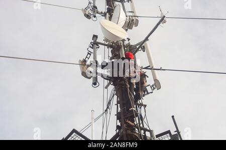 Elettricista uomo o alpinista arrampicata su palo antenna per ispezione Foto Stock