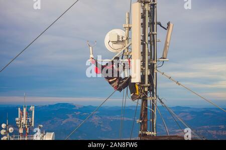 Elettricista uomo o alpinista arrampicata su palo antenna per ispezione Foto Stock