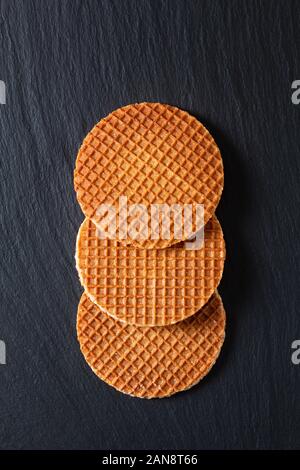 Concetto di cibo Stroopwafel, croccante caramello sciroppo cialde olandese su ardesia nera sullo sfondo di pietra Foto Stock