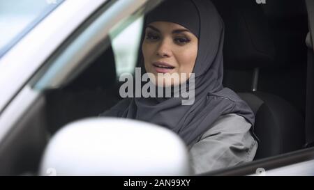 Giovani Musulmani lady cercando in specchio retrovisore seduti in auto, in preparazione alla guida Foto Stock