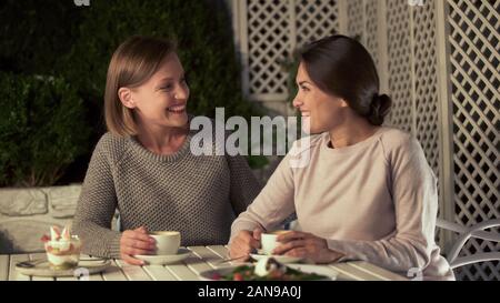 Donna sorridente amici alla ricerca di ogni altro, rilassante in cafe con tazze di tè Foto Stock