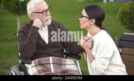 Preoccupato per il giovane donna consolante malati nonno seduto nella sedia a rotelle, ospedale Foto Stock