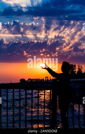 Silhouette di donna. Una donna che prende il sole con le mani su un luminoso Nuvoloso Tramonto sullo sfondo. Estate Mare fotografia in Ucraina Foto Stock