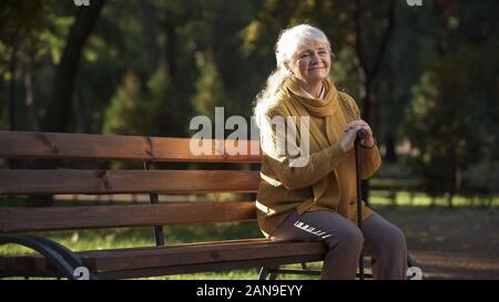 Felice di età donna godendo calda giornata di sole seduto sulla panchina nel parco, il pensionamento Foto Stock