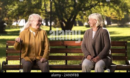 Due anziane signore ridendo e parlando, seduti su una panchina nel parco, vecchi amici Foto Stock