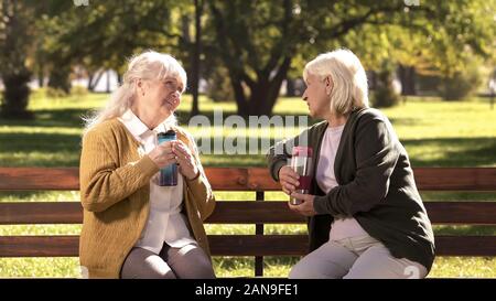 Due vecchi signori di bere il tè caldo da tazze, seduti su una panchina nel parco di sole Foto Stock