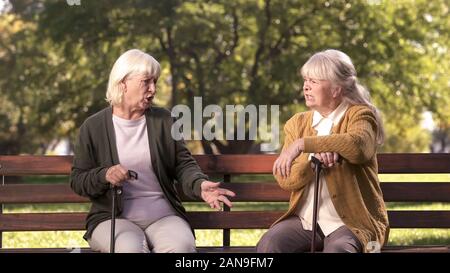 Due anziani signori sostenendo e sedersi sulla panchina nel parco, scontroso anziani, controversia Foto Stock