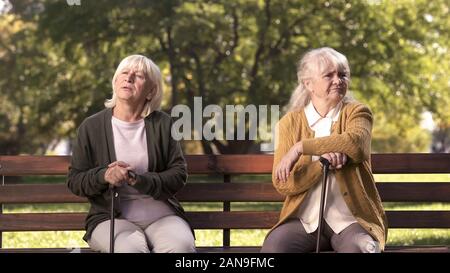 Coppia ladies seduta separatamente sulla panchina nel parco, amici hanno sostenuto e oggetto di contesa Foto Stock