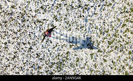 Vista aerea di una ragazza sul campo in erba ricoperta di neve in piedi e a diffondere il suo braccio e guardando alla propria ombra. Vista superiore da un drone Foto Stock