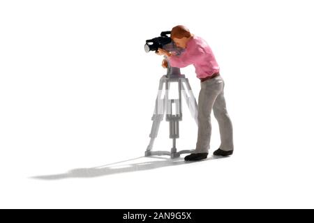 Il cameraman in miniatura di lavorare con la telecamera su un treppiede, le riprese di una scena. Piccola persona isolato su sfondo bianco con lunga ombra Foto Stock