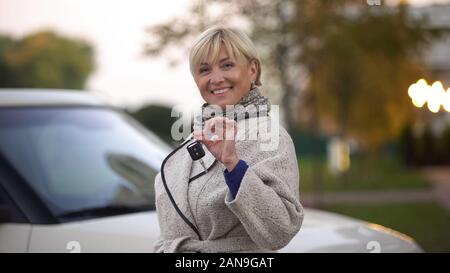 Successo matura donna sorridente e tenendo premuto i tasti delle nuove auto di lusso, presente Foto Stock