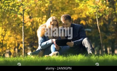 Giovane lo shopping online, utilizzando tablet in autunno park, comprare dei vestiti caldi in net Foto Stock