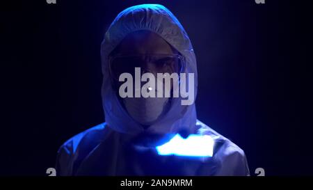 Scienziato maschio in maschera protettiva e occhiali su sfondo scuro, professione Foto Stock