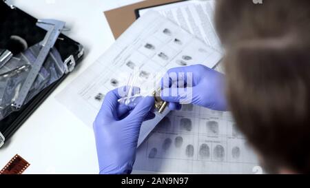 Detective maschio indossando i guanti esaminando i proiettili dalla scena del crimine in office Foto Stock