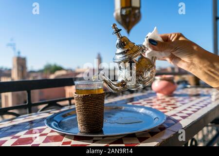 Versando tè marocchino da argento bollitore per il vetro sul tetto di Marrakech, Marocco Foto Stock
