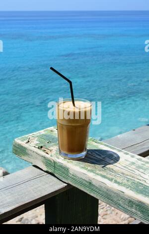 Il greco Frappé, caffè ghiacciato con paglia su grunge di legno verde resto contro il mare blu sfondo in ahot, giornata di sole Foto Stock