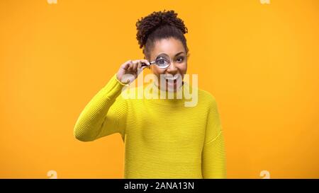 Felice femmina nero guardando la telecamera attraverso la lente di ingrandimento, sconvolgente notizia, ricerca Foto Stock