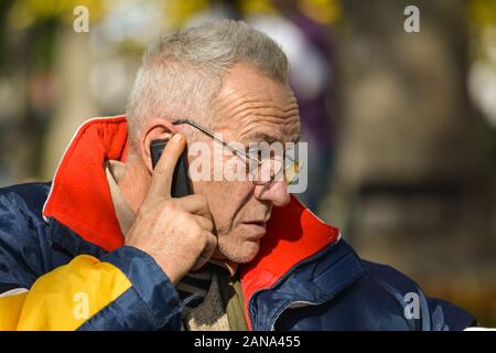 Buona ricerca senior attivo concentrato su notizie importanti durante la chiamata telefonica in luminose, suuny giornata autunnale, vista ravvicinata Foto Stock