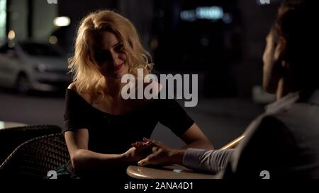 Donna felice tenendo la mano mans, seduta in ristorante, amore confessione, data Foto Stock
