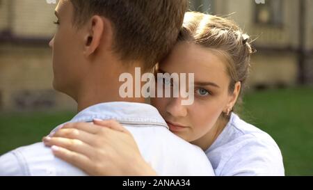 Triste teen ragazza abbracciando il fidanzato e guarda la fotocamera, difficoltà di relazione Foto Stock