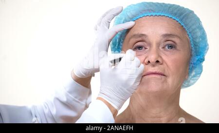 Un chirurgo plastico segni di disegno sulla vecchia donna faccia prima di anti-invecchiamento della terapia Foto Stock