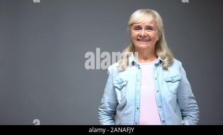 Vecchia signora sorridente nella fotocamera, sembra sano e alla moda di casual abbigliamento denim Foto Stock