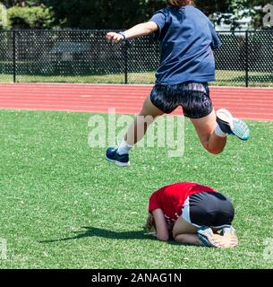 Una scuola di alta via e atleta di campo ostacoli il suo compagno di squadra durante una partita di rana di salto ad una pratica divertente giorno d'estate. Foto Stock