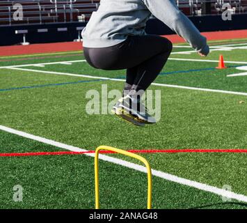 Una pista e campo atleta salta sopra un mini giallo ostacolo per una giornata di sole durante la via e la pratica sul campo. Foto Stock