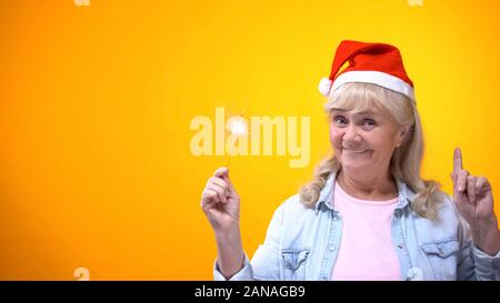 Emozionato anziana signora azienda luci di bengala celebrare la vigilia di Natale, sfondo Foto Stock