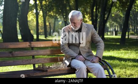 Uomo maturo preparando la scacchiera per il gioco seduta sul banco in park, il pensionamento Foto Stock